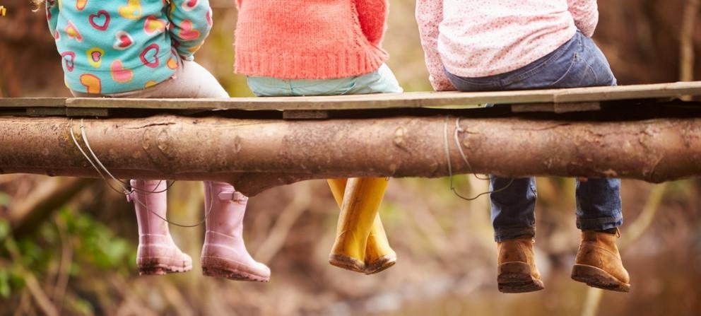 Kinder in Gummistiefeln, sitzend auf Baumstamm