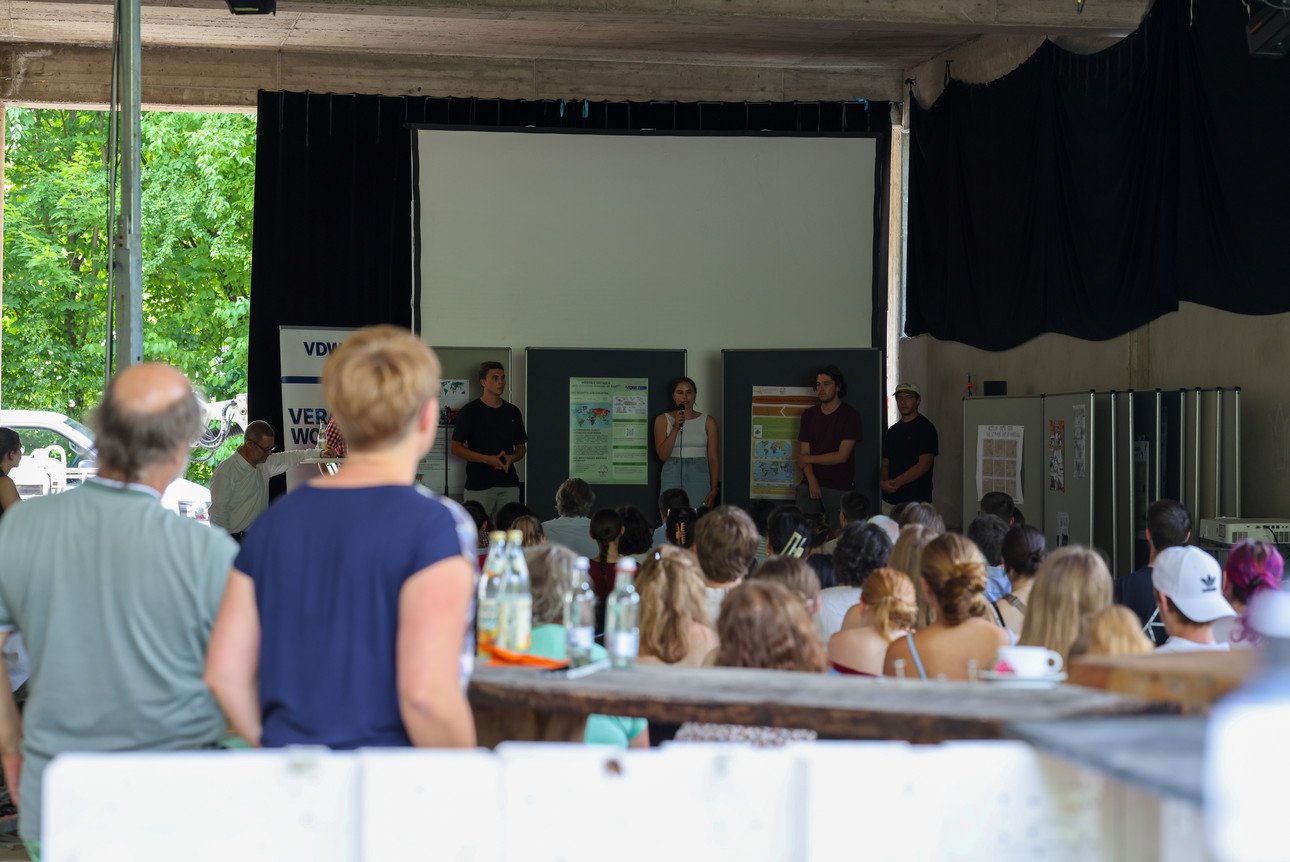 Studierende tragen im Sommersemester 2025 auf einer B&uuml;hne im Kulturtransport an der Universit&auml;t Passau vor gro&szlig;em Publikum &uuml;ber die Ergebnisse ihrer Arbeiten im Rahmen der Veranstaltung "Grenzen &uuml;berwinden" vor.