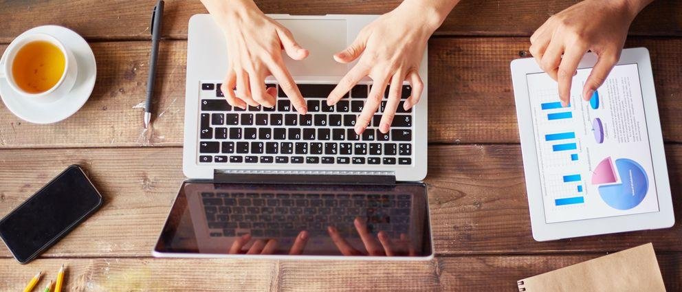 Wooden desk with coffee cup, laptop and tablet Wooden desk with coffee cup, laptop and tablet on which hands are typing