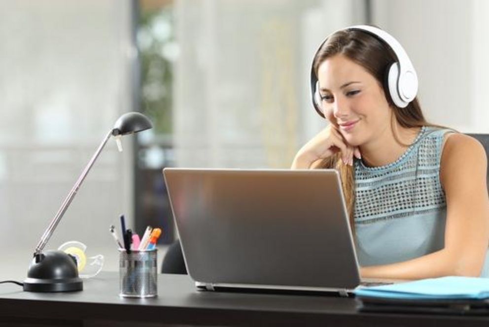 Symbolbild: junge Frau mit Kopfhörern sitzt vor einem Laptop