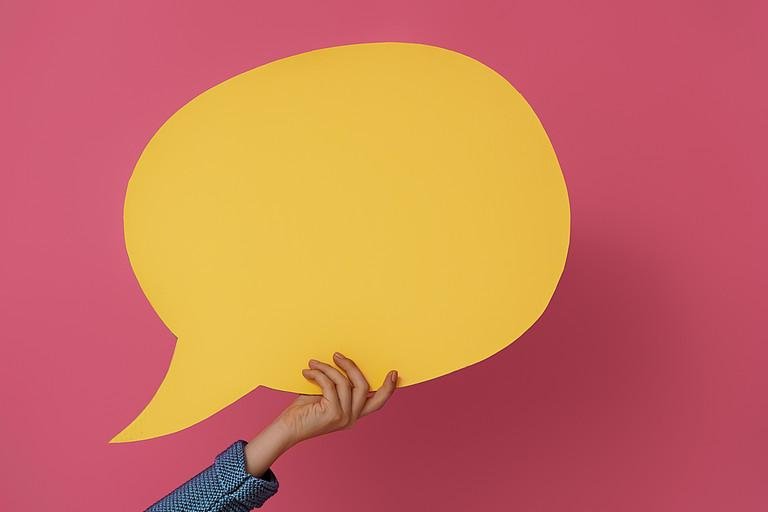 yellow speechbubble being held up in front of a red screen