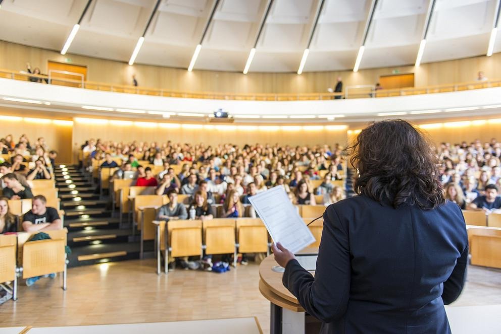 Symbolbild: Professorin redet im Hörsaal zu Student:innen