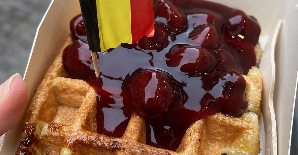 Das Bild zeigt eine Waffel mit Kirschen und einem Fähnchen mit der belgischen Flagge