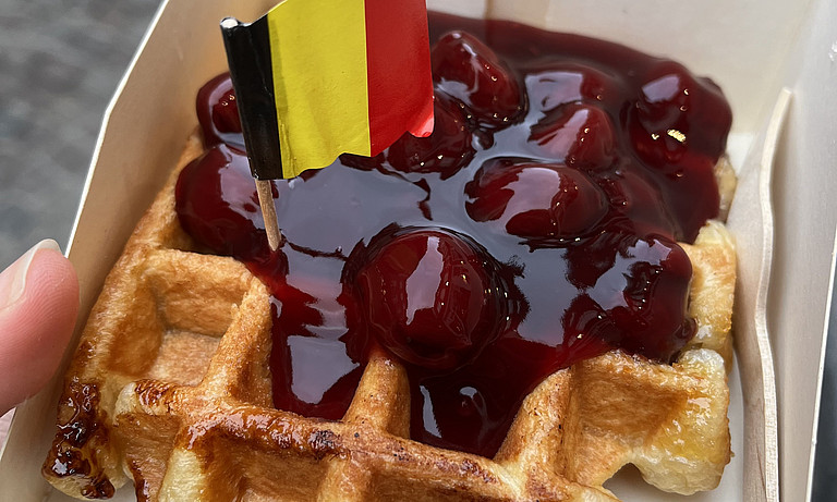 Das Bild zeigt eine Waffel mit Kirschen und einem Fähnchen mit der belgischen Flagge