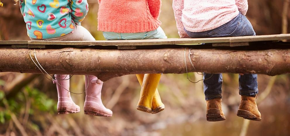 Kinder sitzend auf Baumstamm, in Gummistiefeln