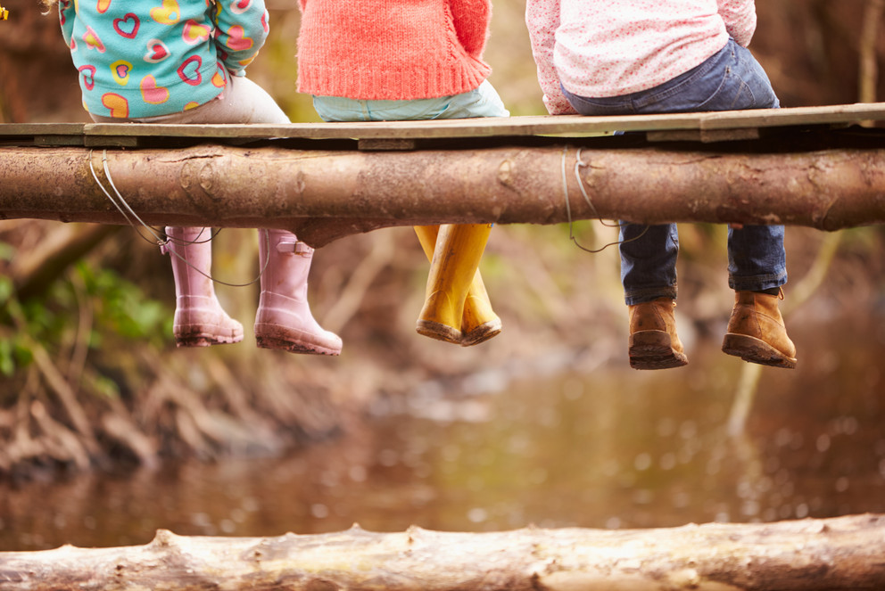 Children's feet in wellies dangling from a building trunk