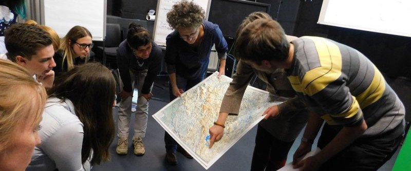 Studierende und Dozierende im Kreis um einen gro&szlig;e Landkarte