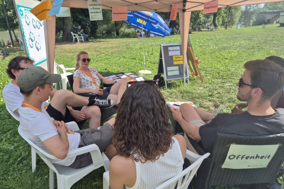 Gruppe von 5 Leuten sitzt auf Gartenst&uuml;hlen im Halbkreis und ist im Gespr&auml;ch