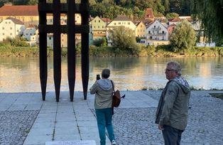 [Translate to Tschechisch:] Denkmalansicht mit Blickrichtung Inn bei abendlichem Licht aus ca. 10m Entfernung, mit zwei Besuchern davor.