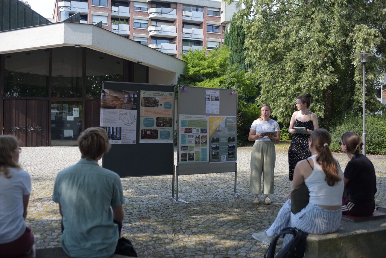 Studierende pr&auml;sentierne ihre Seminarergebnisse vor der ehm. Kirche Christi Himmelfahrt anhand eines ausgedruckten Plakates. 