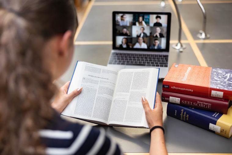 Studentin liest die Bibel vor dem Laptop