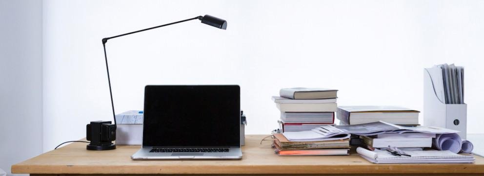 Ein Schreibtisch mit Büchern, Laptop und Lampe.