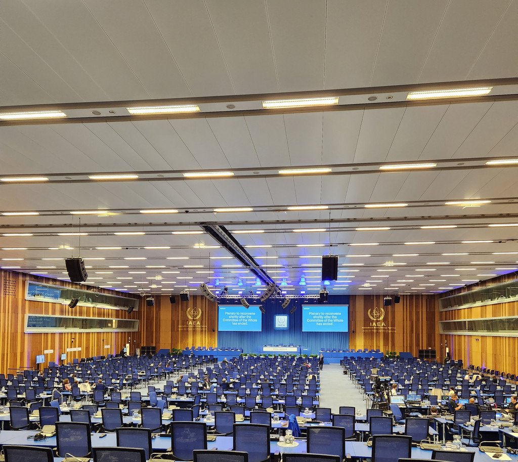 Großer Konferenzsaal der UNO in Wien mit vielen Plätzen, Mikrofonen und Bildschirmen.