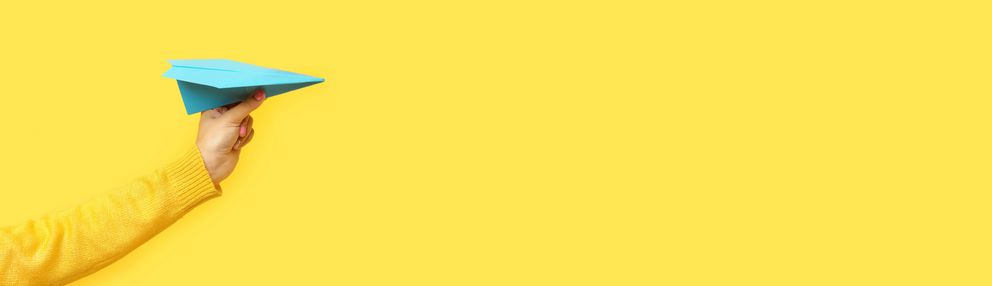 Mintfarbener Papierflieger vor gelbem Hintergrund