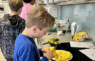 Ein Kind schneidet an einer Küchenanrichte Mango.