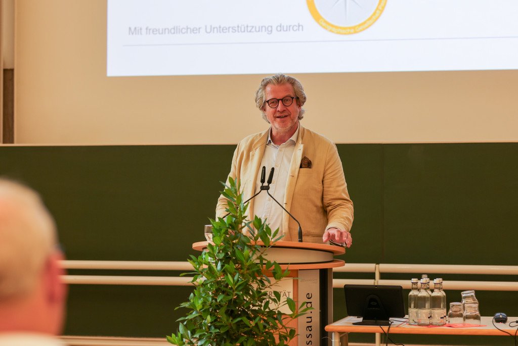 Der Journalist Dr. Philipp Blom steht an einem Rednerpult im Audimax der Universität Passau im spricht vor Publikum über das Verhältnis von Mensch und Natur.
