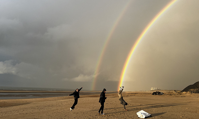 Das Bild zeigt drei Menschen unter einem doppelten Regenbogen