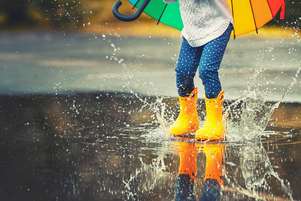Feet of a child in yellow rubber boots jumping over a puddle in the rain