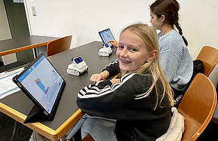 Zwei Kinder sitzen vor Tablets und programmieren mithilfe einer speziellen App Roboter.