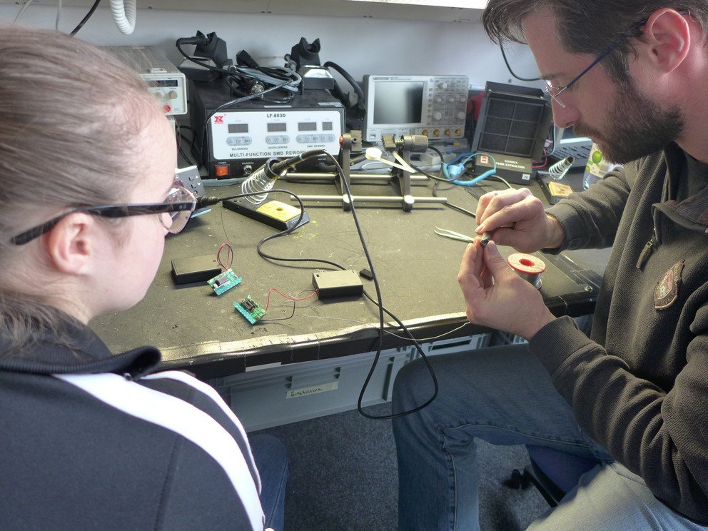 Professor Matthias Kranz vom Lehrstuhl für Informatik mit Schwerpunkt Eingebettete Systeme bastelt mit einer Schülerin ein elektronisches Gerät, mit dem sie Texte in die Luft schreiben kann.