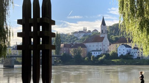 [Translate to Tschechisch:] Aufnahme der Skulptur mit Blickrichtung Inn, im Hintergrund die Innstadt mit St. Gertraud und Mariahilfkirche