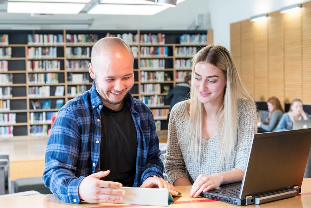 Zwei junge Menschen in einer Bibliothek betrachten gemeinsam ein Tablet.