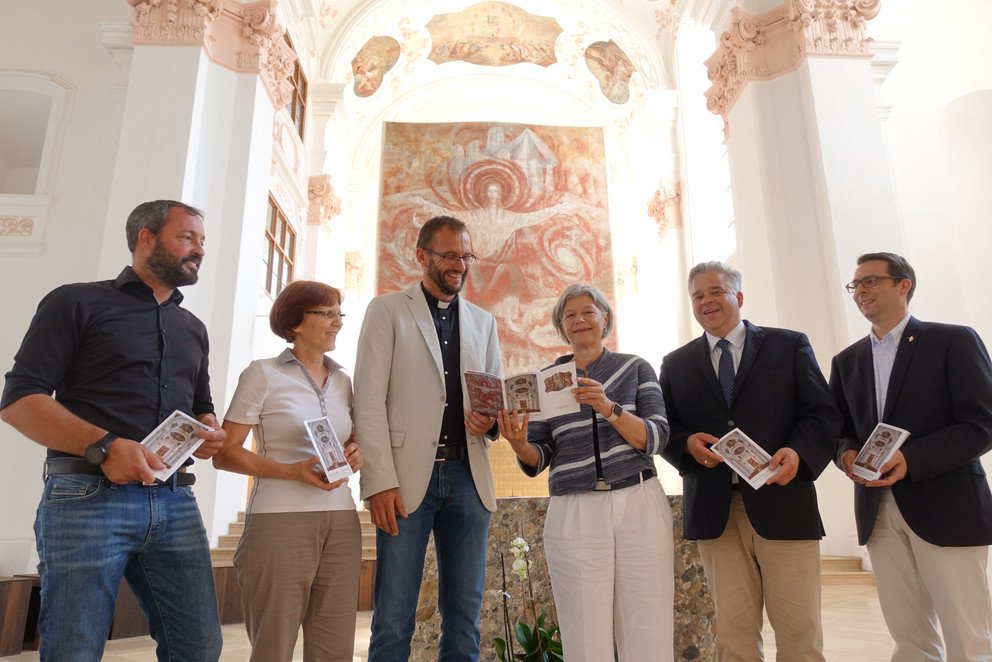 Studierendenpfarrer Andreas Erndl &uuml;bergab gemeinsam mit Verleger und Fotograf Marcel Peda (von links), KSG-Referentin Maria-Theresia Eber und Di&ouml;zesanmusikdirektor Marius Schwemmer (rechts) den neuen Kirchenf&uuml;hrer an Pr&auml;sidentin Prof. Dr. Carola Jungwirth und Kanzler Dr. Achim Dilling.