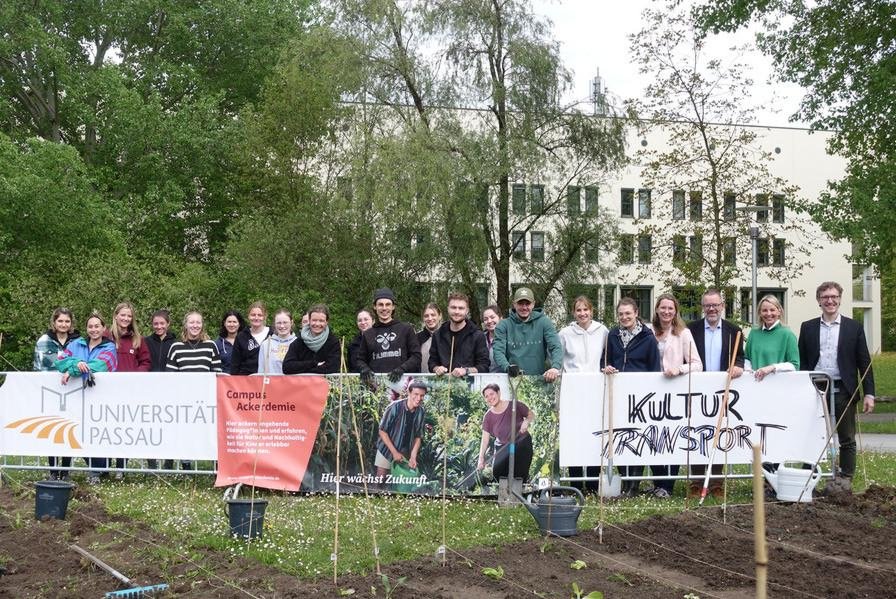 Das Team der CampusAckerdemie steht mit Plakaten der Universität Passau und des Kulturtransports am Acker auf dem Campus der Universität Passau