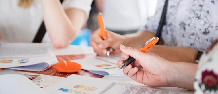 Zwei Studierende, die Stifte in der Hand halten und sich einschreiben.