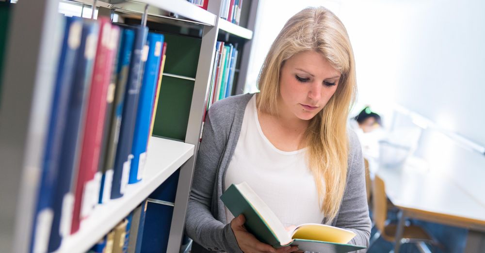 Studentin in der Bibliothek mit einem Buch