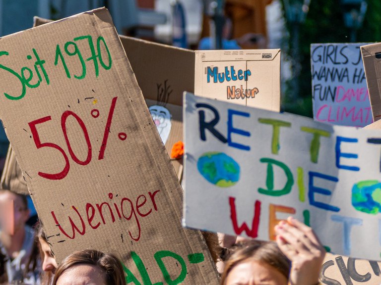 Demonstrierende auf einer Fridays-for-Future-Demonstration halten bunte Schilder für den Klimawandel hoch.