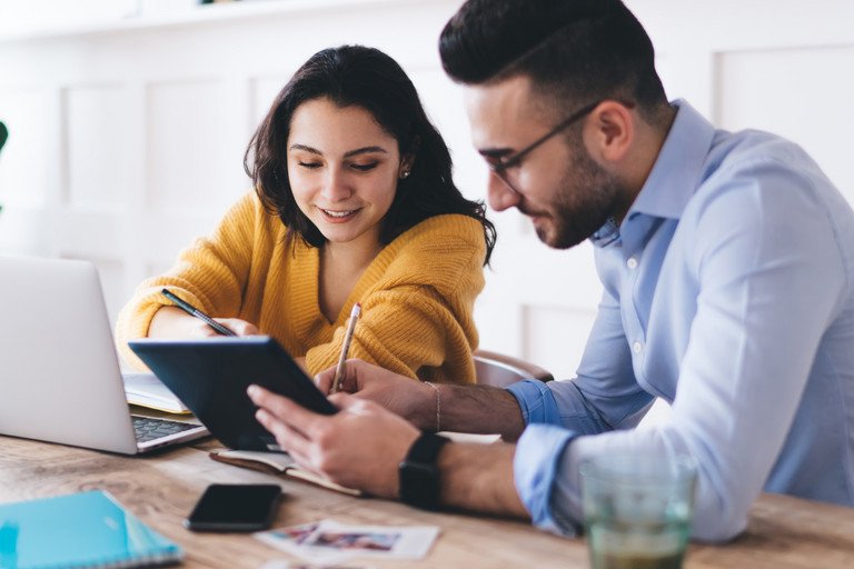 Ein junger Mann und eine Junge Frau blicken auf ein Tablet. Es handelt sich um eine Lern- oder Arbeitsumgebung