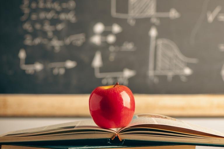 Apfel auf einem Buchstapel vor einer Schultafel 