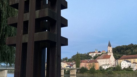 [Translate to Tschechisch:] Ansicht der Skulptur aus etwa 5m Entfernung mit Blickrichtung Inn, im Hintergrund zu sehen die Kirche St. Gertraud