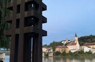 Ansicht der Skulptur aus etwa 5m Entfernung mit Blickrichtung Inn, im Hintergrund zu sehen die Kirche St. Gertraud