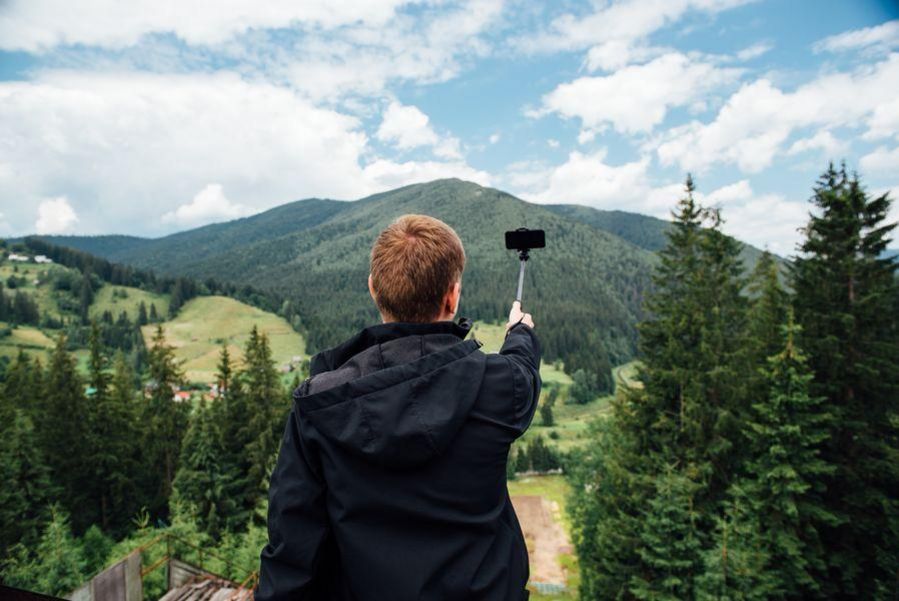 Junge mit Selfiestick vor Bergregion
