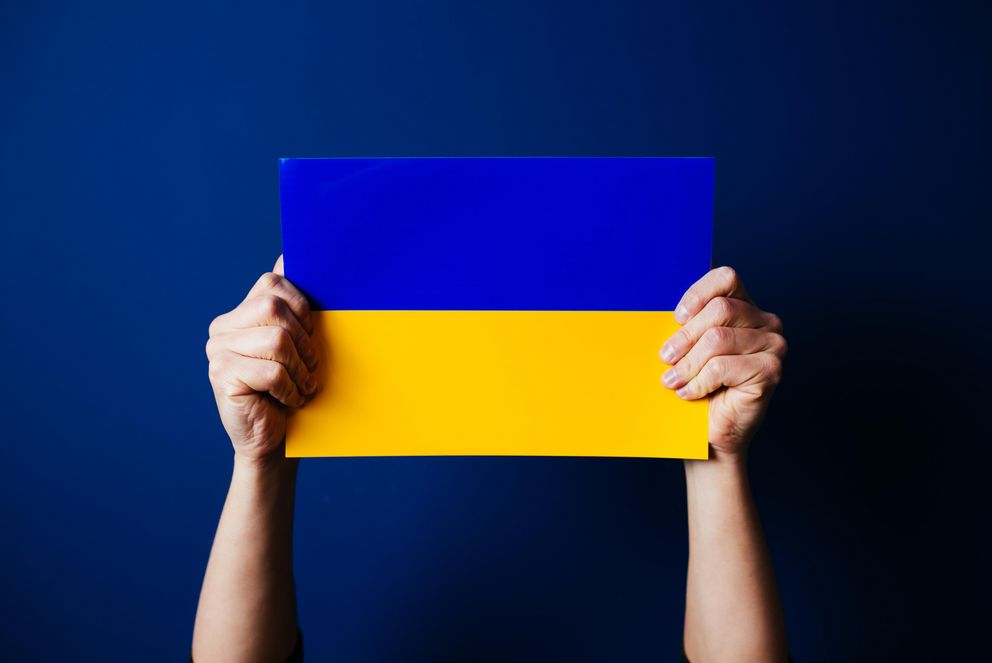 Zwei Hände halten eine kleine ukrainische Flagge in die Höhe.