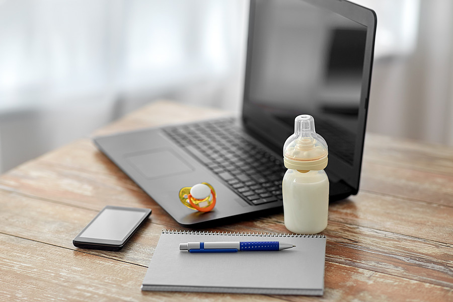 Laptop, Notizbuch, Schnuller und Babyflasche auf einem Tisch