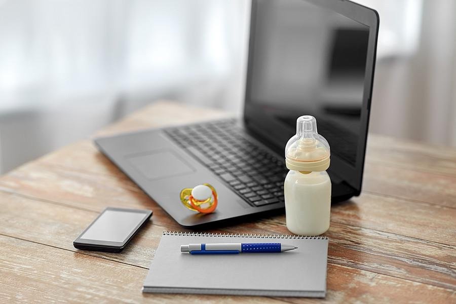 Laptop, Notizbuch, Schnuller und Babyflasche auf einem Tisch