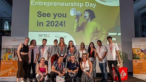 Gruppenbild aller Teilnehmenden auf der Bühne, im Hintergrund ist eine Folie aufgelegt, die den 1. Platz verkündet.