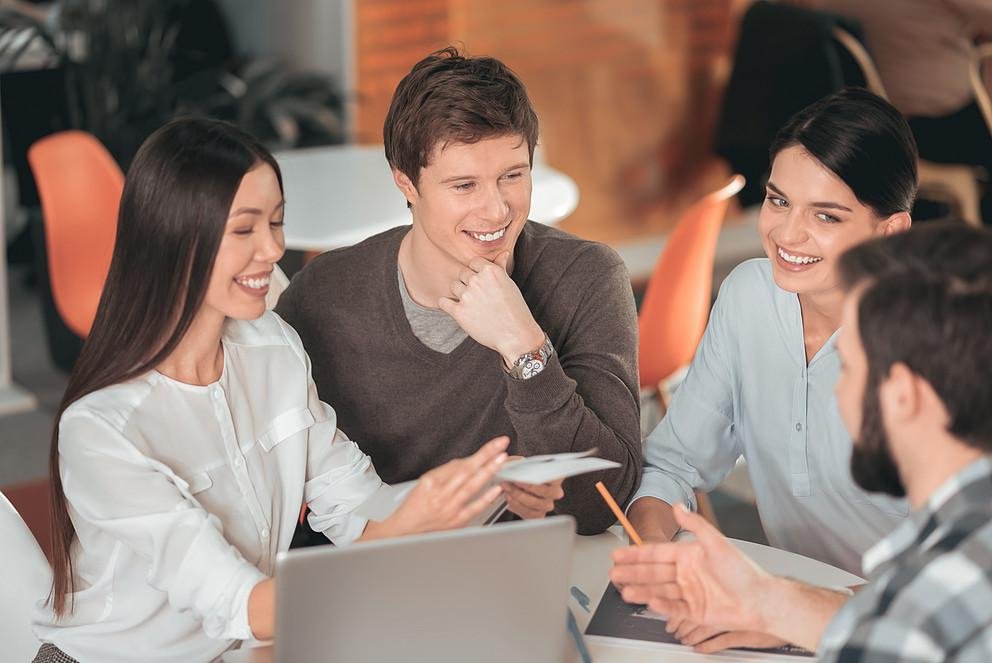 Eine Grupppe bestehend aus jeweils zwei Doktorandinnen und zwei Doktoranden sitzen zusammen in der Cafete der Mensa und unterhalten sich über einen gemeinsamen Workshop, den sie organisieren wollen. Auf dem Tisch steht ein geöffneter Laptop, eine Doktorandin macht Notizen.