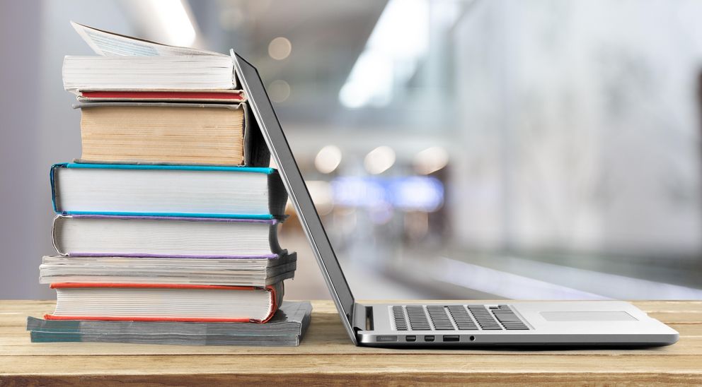 Stack of books with laptop on wooden table