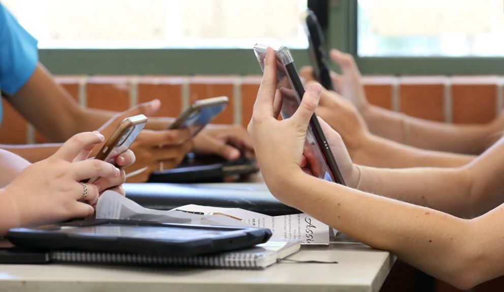 Schüler und Schülerinnen arbeiten mit Tablets und Smartphones an einem Schreibtisch.