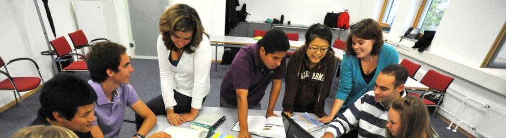 Studierende über einen Tisch gebeugt Studierende über einen Tisch gebeugt