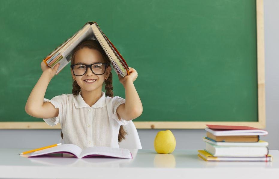 Schulmädchen mit einem Buch über dem Kopf