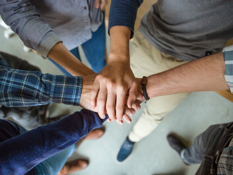 Menschen stehen in einem Kreis und legen die Hände übereinander.