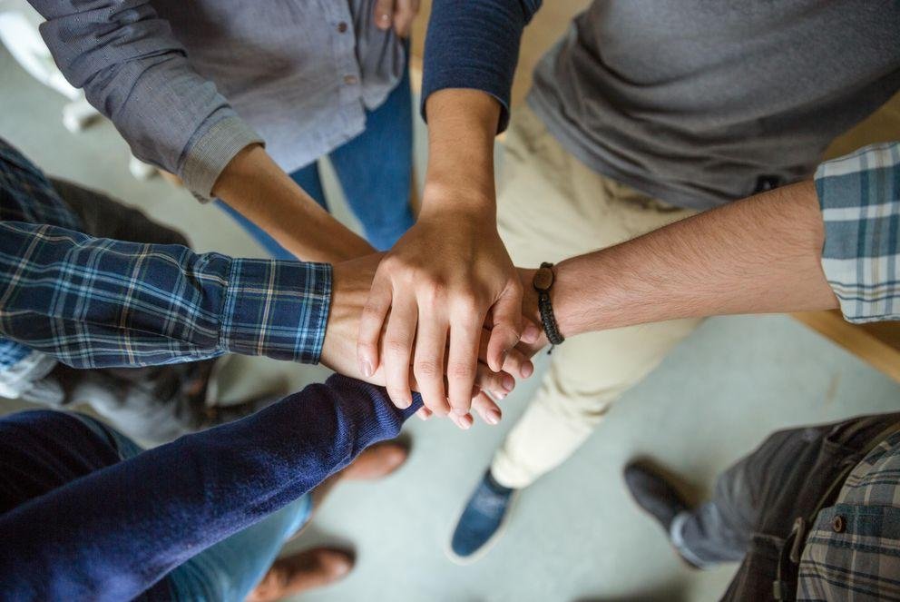 Menschen stehen in einem Kreis und legen die Hände übereinander.