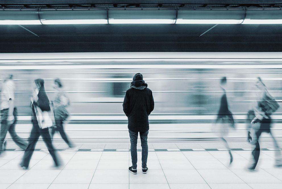 Stehende Person von hinten und vorbeigehende, verwischte Personen an einer U-Bahn-Station. Symbolfoto: Adobe Stock