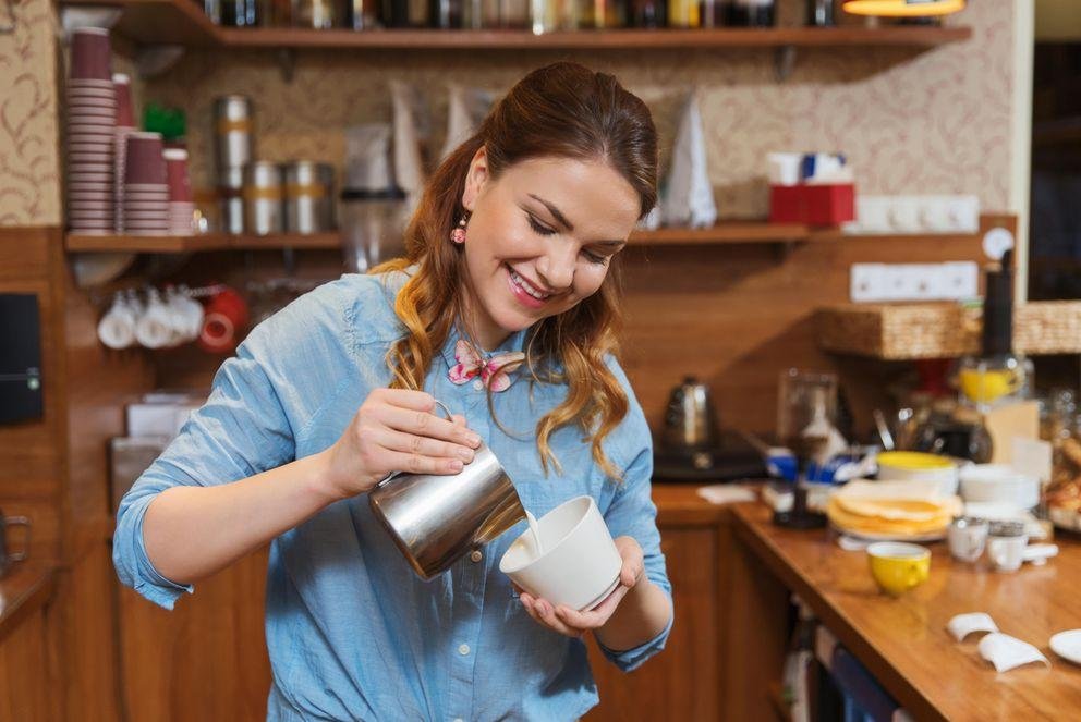 barista woman pouring cream to cup at coffee shop