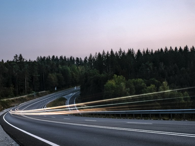 Lichter des Autoverkehrs auf einer Landstraße in der Abenddämmerung als Symbolbild für Mobilität im ländlichen Raum..